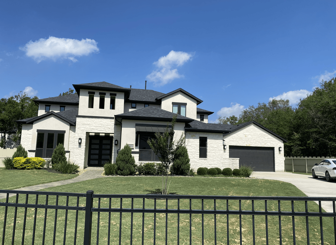 A modern home with a landscaped front yard, featuring greenery and a black fence.